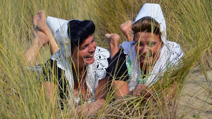 Zeeuwse-meisjes-in-klederdracht-liggen-tussen-het-helmgras-in-de-duinen-foto-Mirjam-Kempkes-uit-Koudekerke